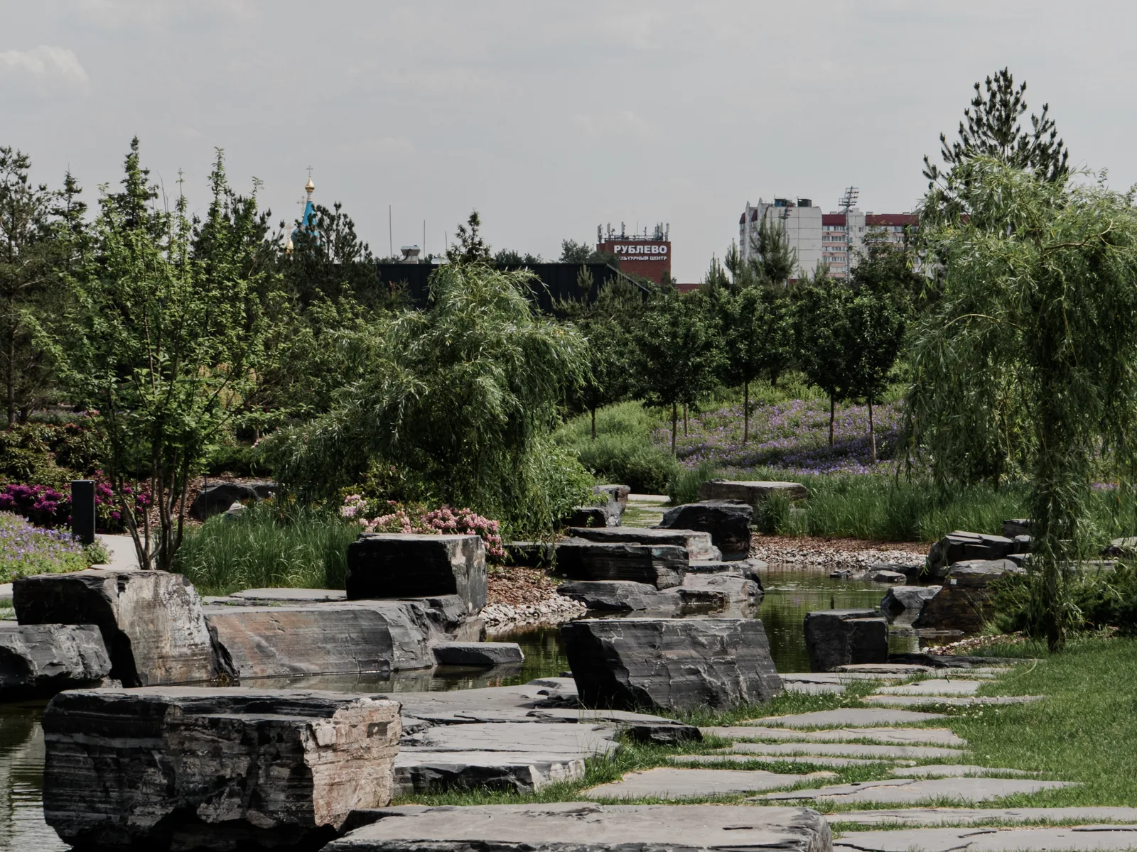 A stream in a city park: banks and passages made of shungite blocks, willows and flower beds along the water’s edge